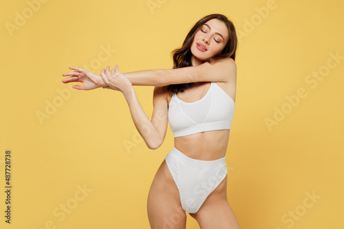 Tender calm slim lovely attractive young brunette woman 20s in white underwear with beautiful perfect fit body standing posing close eyes isolated on plain yellow colot background studio portrait photo