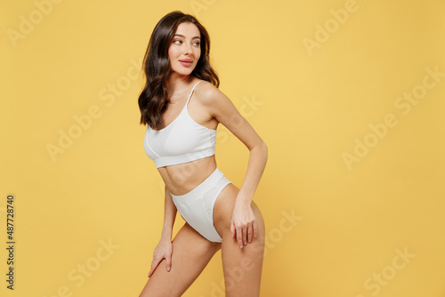 Seductive stunning confident sexy lovely attractive young brunette woman 20s in white underwear with perfect fit body stand posing look aside on workspace isolated on plain yellow background studio photo