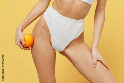 Cropped close up photo young caucasian woman 20s in white underwear with perfect fit body holding orange fruit isolated on plain yellow background studio portrait. People lifestyle bodycare concept
