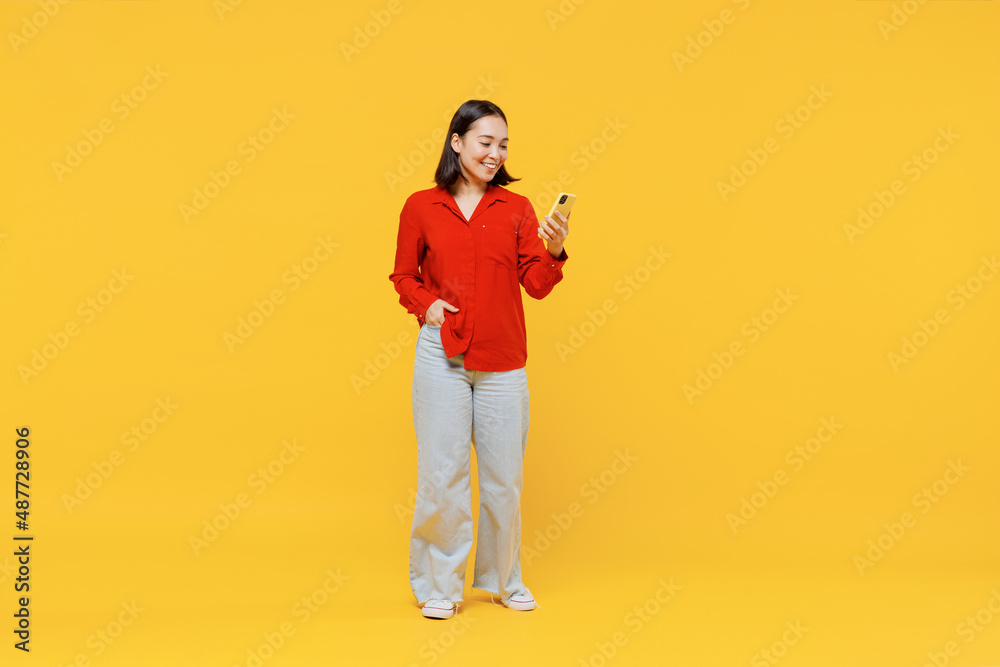 Full size body length vivid marvelous magnificent young woman of Asian ethnicity 20s years oldin casual clothes hold in hand use mobile cell phone isolated on plain yellow background studio portrait. Full size body length vivid marvelous magnificent young woman of Asian ethnicity 20s years oldin casual clothes hold in hand use mobile cell phone isolated on plain yellow background studio portrait.