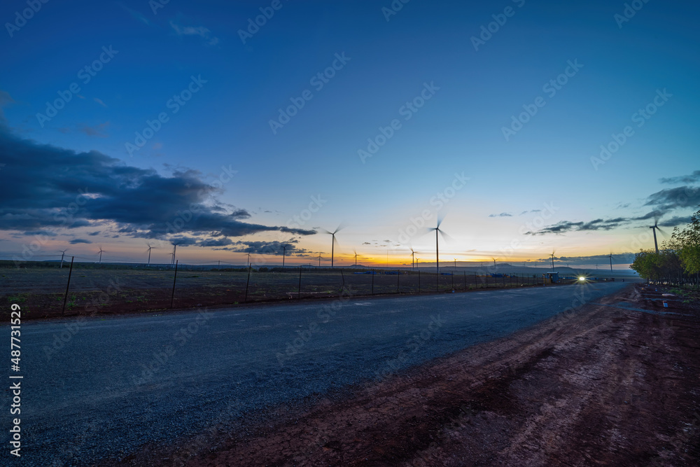 Wind turbine farm and agricultural fields on a summer day. Wind electricity generator in sunset sky, power plant, wind efficiency.