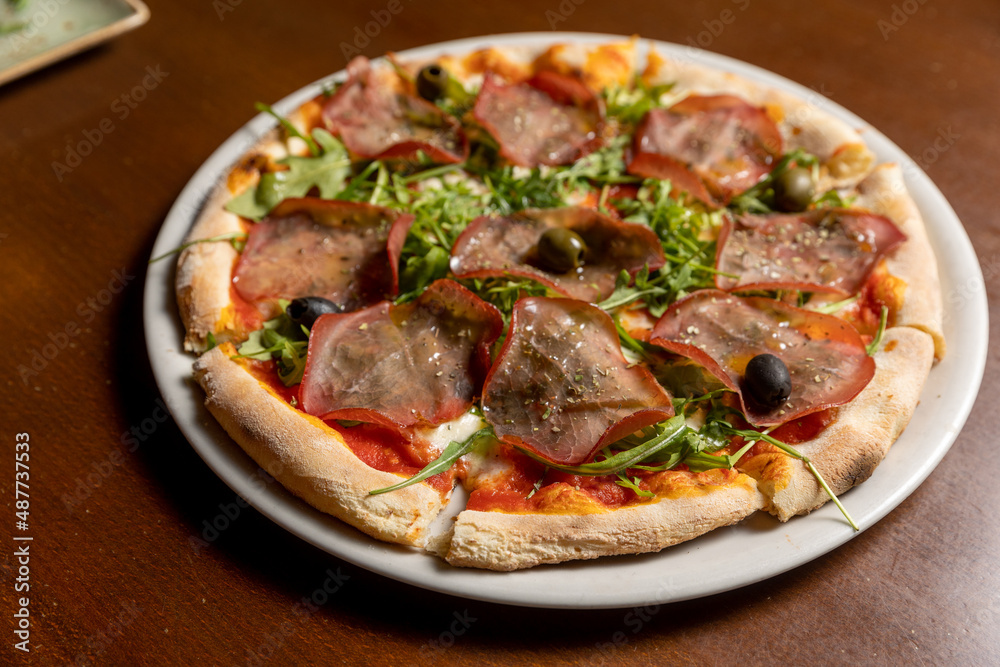 Arugula prosciutto pizza served on white plate Arugula prosciutto pizza served on white plate