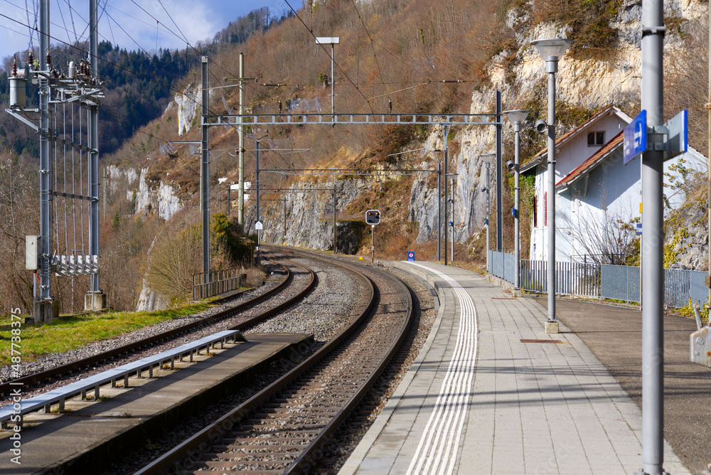 Railway tracks with platform at railway station of St-Ursanne on a cloudy winter day. Photo taken February 7th, 2022, Saint-Ursanne, Switzerland.