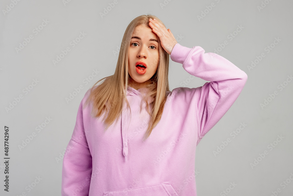 Yikes, oops. Young blonde woman wears violet hoody, stands against grey background surprised with hand on head for mistake, remember error. Forgot, bad memory concept Yikes, oops. Young blonde woman wears violet hoody, stands against grey background surprised with hand on head for mistake, remember error. Forgot, bad memory concept