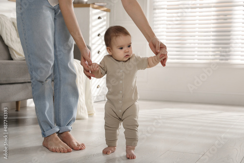 Φωτογραφία Mother supporting her baby daughter while she learning to walk at home