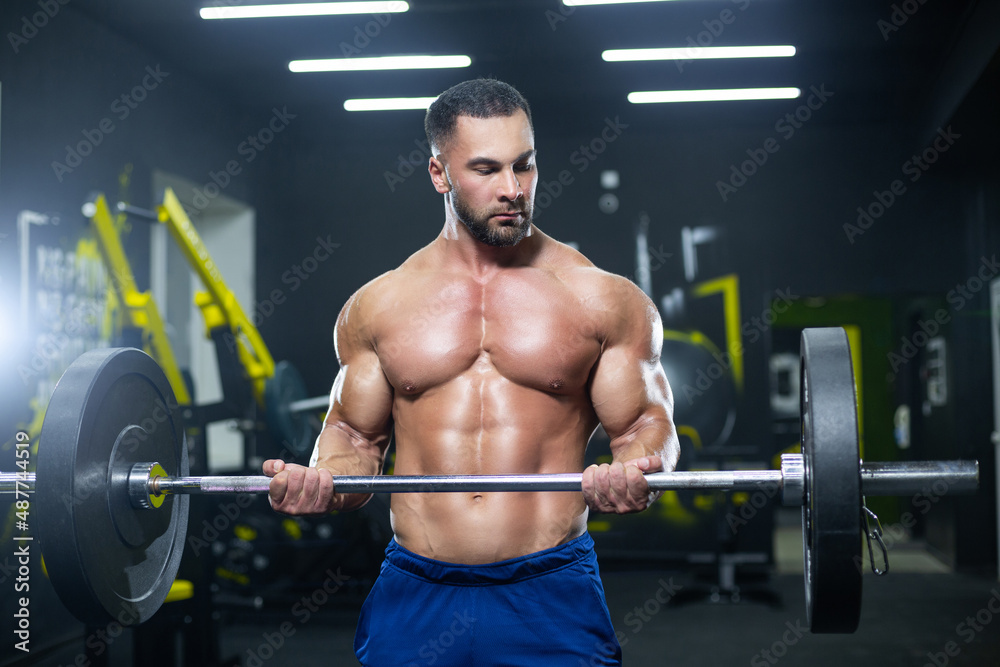 Close up view of a strong muscular athlete lifting heavy barbell showing his muscles in a gym Close up view of a strong muscular athlete lifting heavy barbell showing his muscles in a gym