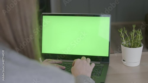 A shot over the shoulder of a business woman typing on a keyboard and looking at a green screen. An office employee using a laptop with a green screen. remote work or training.