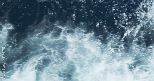 top view of the blue waves cut by a fast ship. Waves quickly disperse from the ship. Close-up