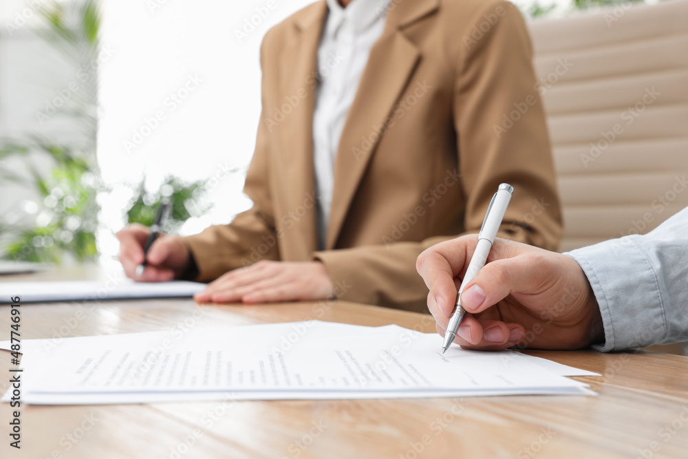 Man signing contract at table in office, closeup. Man signing contract at table in office, closeup.