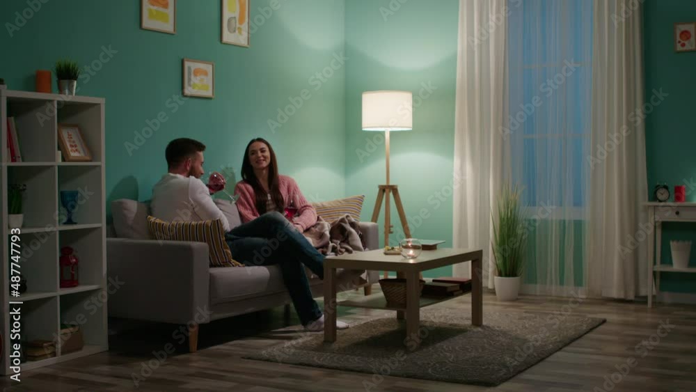 Young couple, man and woman, are relaxing on sofa in cozy living room, drinking some wine and talking, enjoy romantic atmosphere and pleasant communication, Slow motion. Young couple, man and woman, are relaxing on sofa in cozy living room, drinking some wine and talking, enjoy romantic atmosphere and pleasant communication, Slow motion.