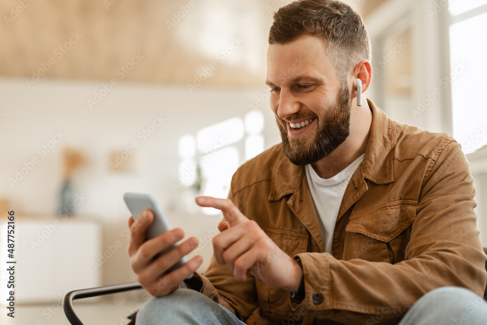 Happy Man Using Mobile Phone Wearing Earbuds Texting At Home Happy Man Using Mobile Phone Wearing Earbuds Texting At Home
