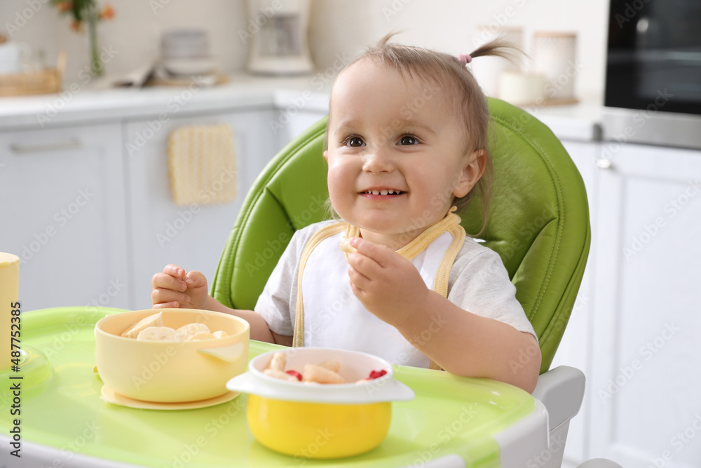 Cute little baby eating food in high chair at kitchen Cute little baby eating food in high chair at kitchen