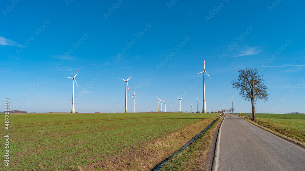 Panoramic view over beautiful farm landscape with early spring agriculture field, wind turbines to produce green energy and a lonely road near Mittweida, Germany, at blue sunny sky.