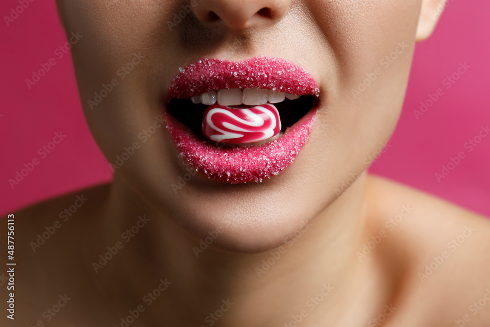 Obraz premium Woman with lips covered in sugar eating candy on pink background, closeup