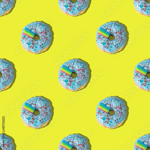 A repeating pattern of blue donuts with a rainbow on a yellow background. Flat lay