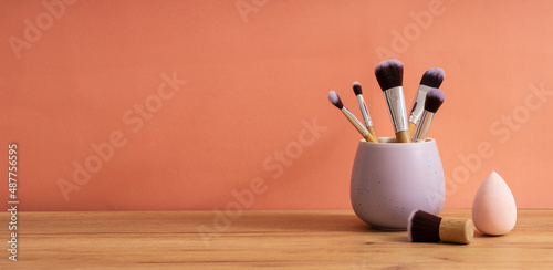 Canvas-taulu Purple organizer full of makeup brushes,sponge for face on the wooden table against bright orange background