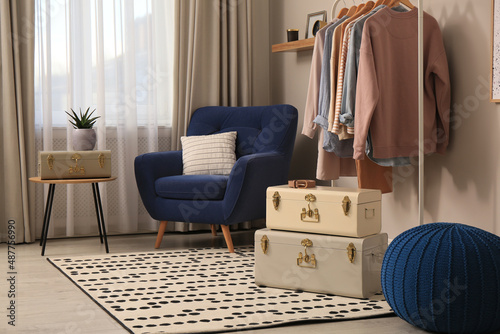 Stylish room interior with comfortable armchair, clothes and storage trunks © New Africa