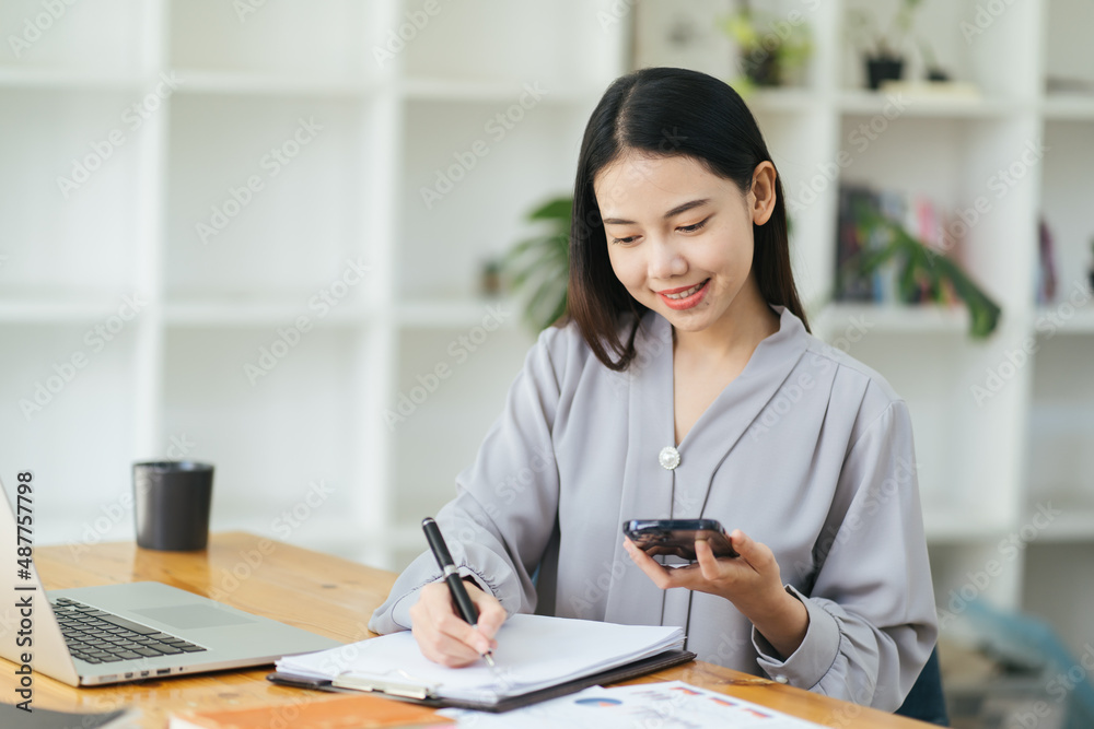 Woman using laptop and smartphone in office. Beautiful girl looking at mobile phone. Entrepreneur, businesswoman, freelance worker, student working on computer at home. Business, technology concept Woman using laptop and smartphone in office. Beautiful girl looking at mobile phone. Entrepreneur, businesswoman, freelance worker, student working on computer at home. Business, technology concept