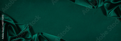Obraz na płótnie Dark green silk satin background. Beautiful soft folds on the smooth surface of the fabric. Luxury background with copy space for design. Wide banner. Top view. Flat lay. w salonie