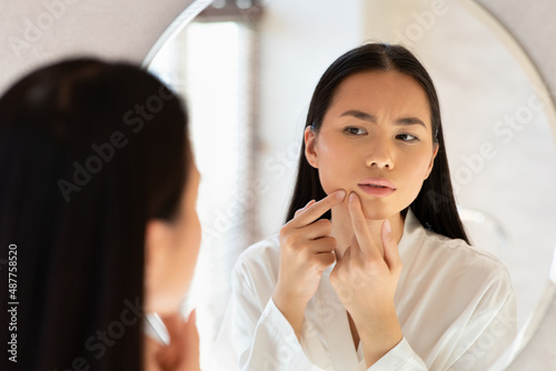 Young asian lady standing in front of mirror, removing blackheads