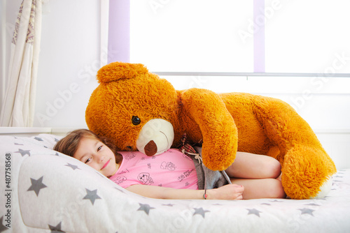 happy young girl playing with her big teddy
