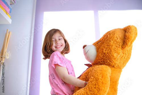 happy young girl playing with her big teddy
