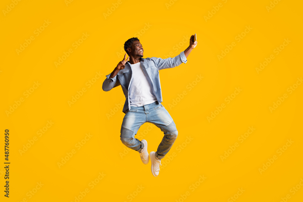 Joyful black guy having fun, taking selfie on smartphone