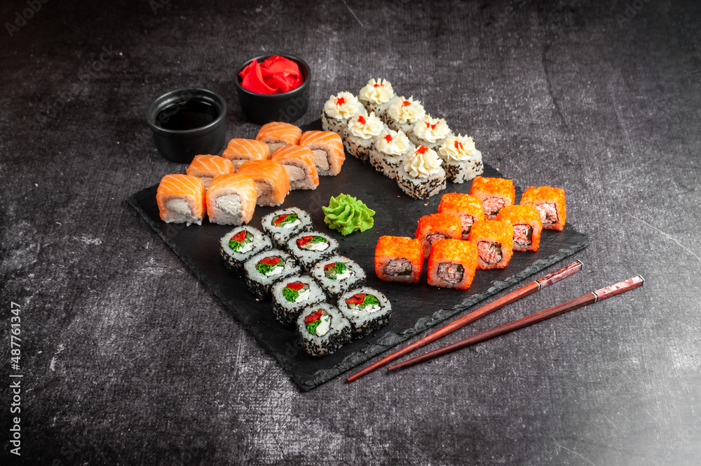 Assorted Japanese sushi on a black board with soy sauce, ginger, wasabi on a gray dark background Assorted Japanese sushi on a black board with soy sauce, ginger, wasabi on a gray dark background