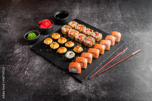 Assorted Japanese sushi on a black board with soy sauce  ginger  wasabi on a gray dark background
