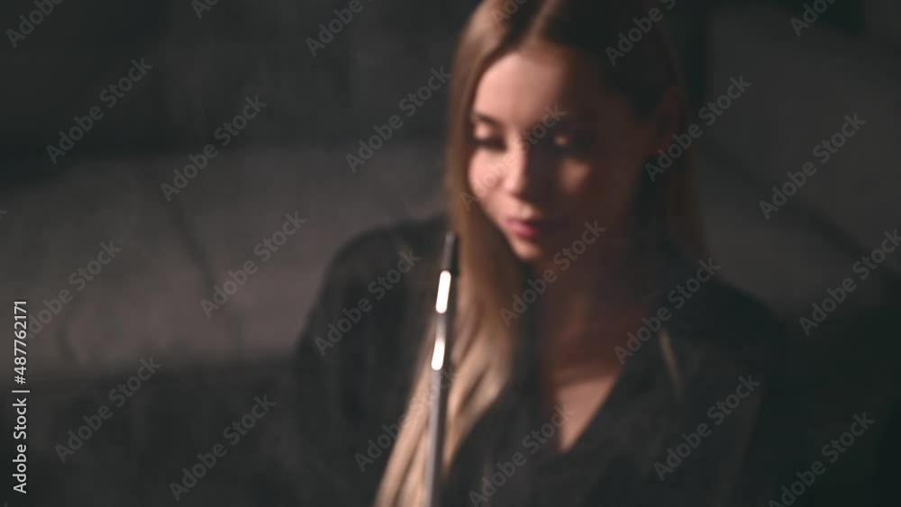 An attractive young adult woman smokes a hookah at home in anticipation of a party with her friends
