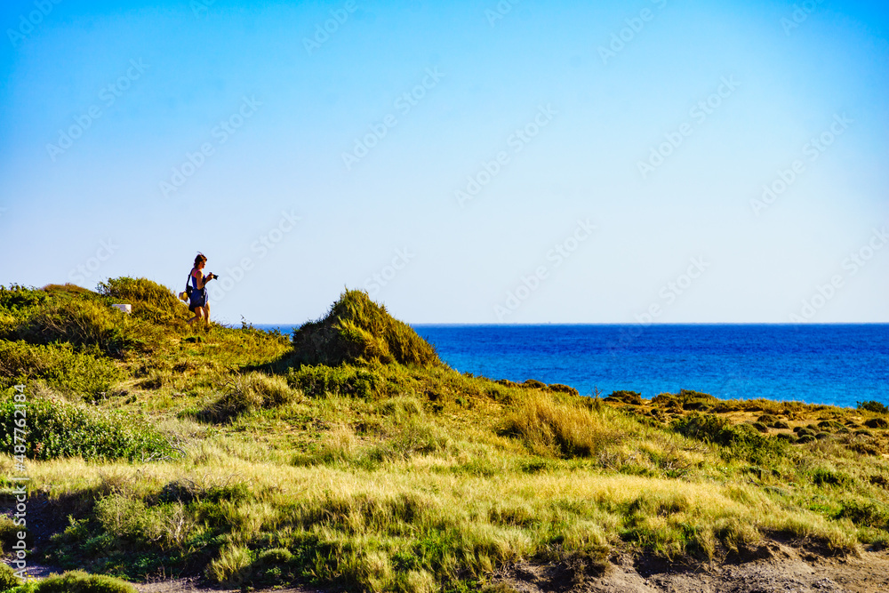 Woman walk on seashore, take photo with camera