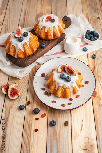 Cake "rum baba" with icing, raisins, blueberries, figs on a light wooden background