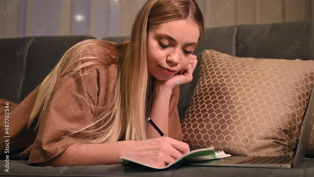 A teenager girl is engaged in homeschooling using a laptop, making notes in a notebook. Study on the couch, distance learning and work A teenager girl is engaged in homeschooling using a laptop, making notes in a notebook. Study on the couch, distance learning and work