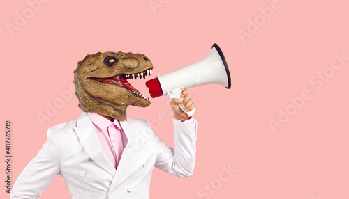 Man wearing dino mask yells in megaphone, side profile view studio portrait. Funny human dinosaur in suit promotes new product, shopping event, invites to party. Scary monster fights for animal rights photo
