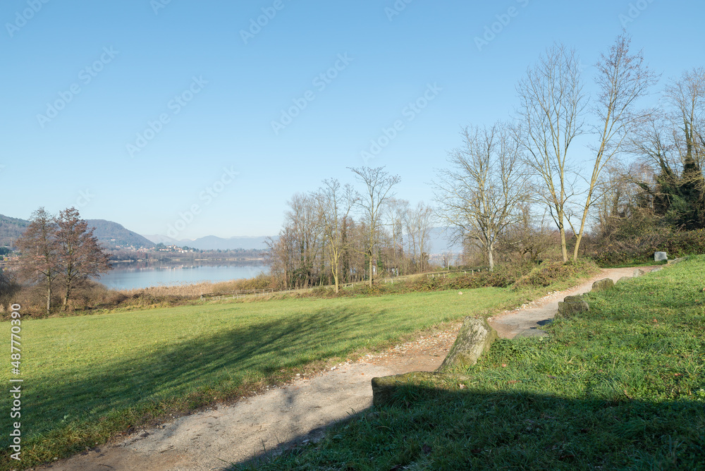 Lake with dirt bike path in winter. Comabbio lake, northern Italy. In the background the town of Comabbio