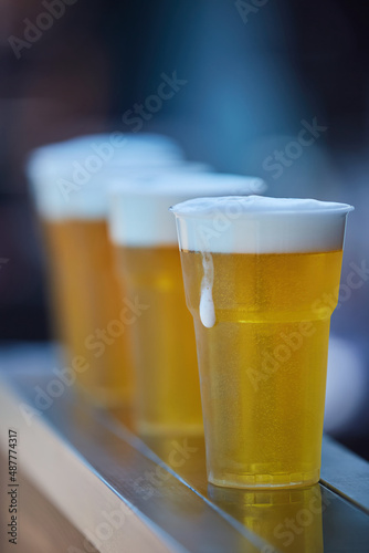 Alcoholic beverage beer in a plastic cup. several glasses in a row. A bar or cafe on the outdoor.