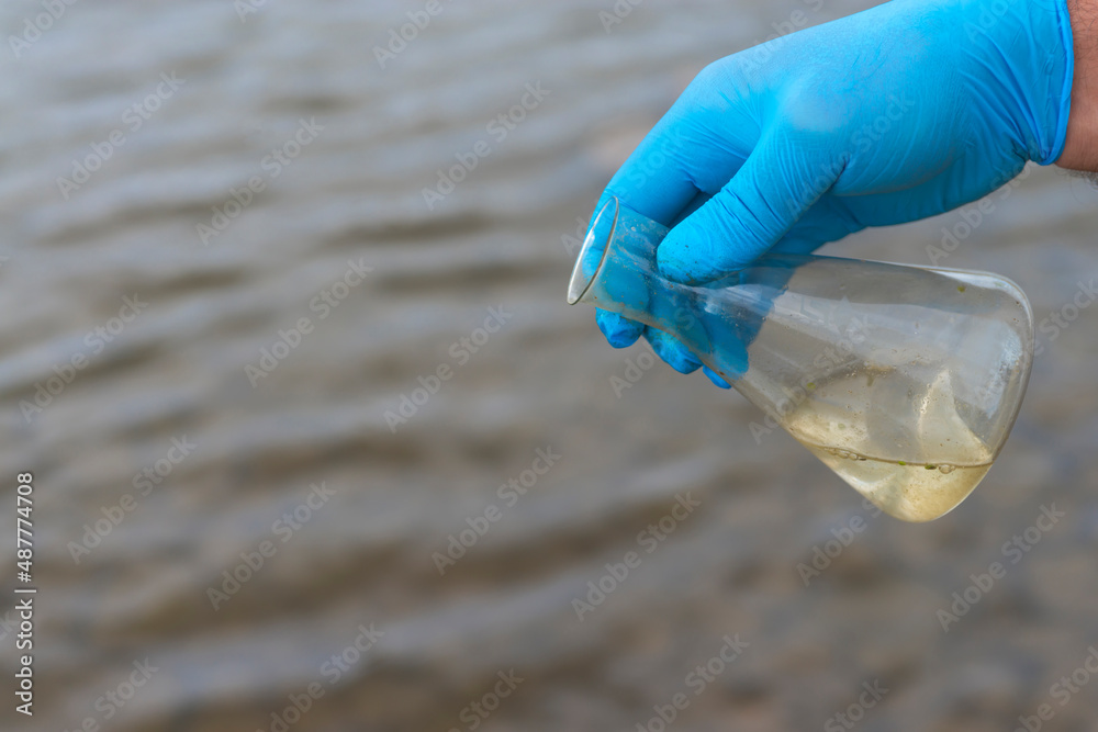 Sample water from the river for analysis. Hand in glove holding a test tube.ecology concept Sample water from the river for analysis. Hand in glove holding a test tube.ecology concept