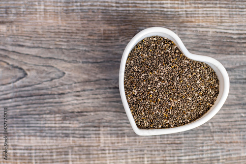 Black chia seeds in a white heart shaped bowl on wooden background. Superfood for healthy eating and diet, contains vitamins and minerals, salvia grains.