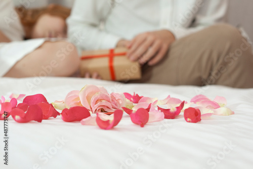 Rose petals in the foreground. The couple in the background give gifts.