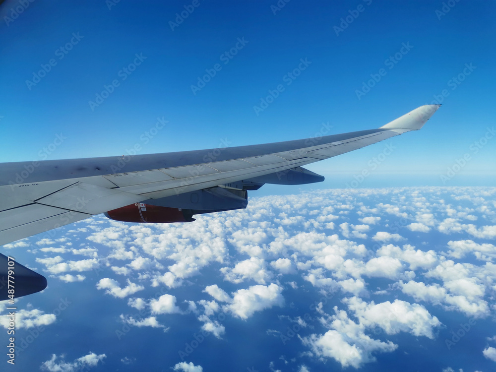 Fototapeta premium View from the porthole on the wing of an airplane with a red aircraft engine flying over beautiful white clouds and the sea.