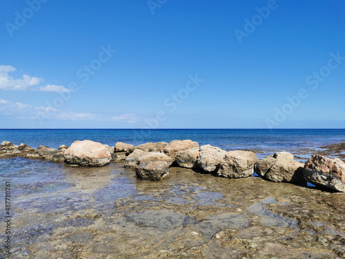 A stone ridge, long-hardened lava, the shore of the Mediterranean Sea against the backdrop of the sea and a blue sky with clouds.