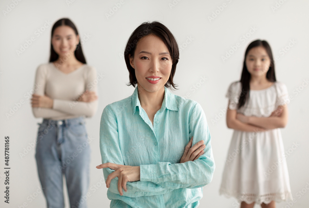 Beautiful mature Asian woman with her adult daughter and granddaughter posing with crossed arms and smiling at camera Beautiful mature Asian woman with her adult daughter and granddaughter posing with crossed arms and smiling at camera