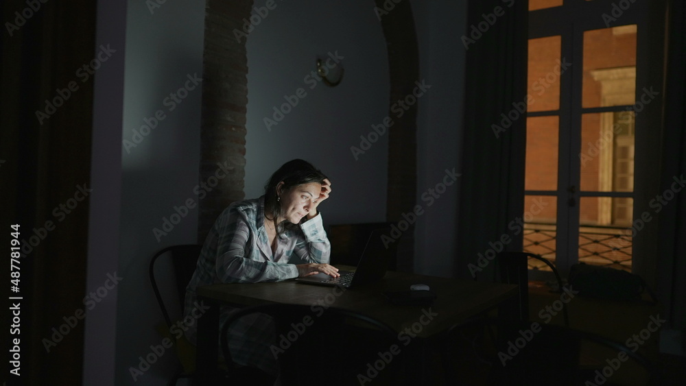 Woman staring at laptop screen at night alone at apartment home Woman staring at laptop screen at night alone at apartment home