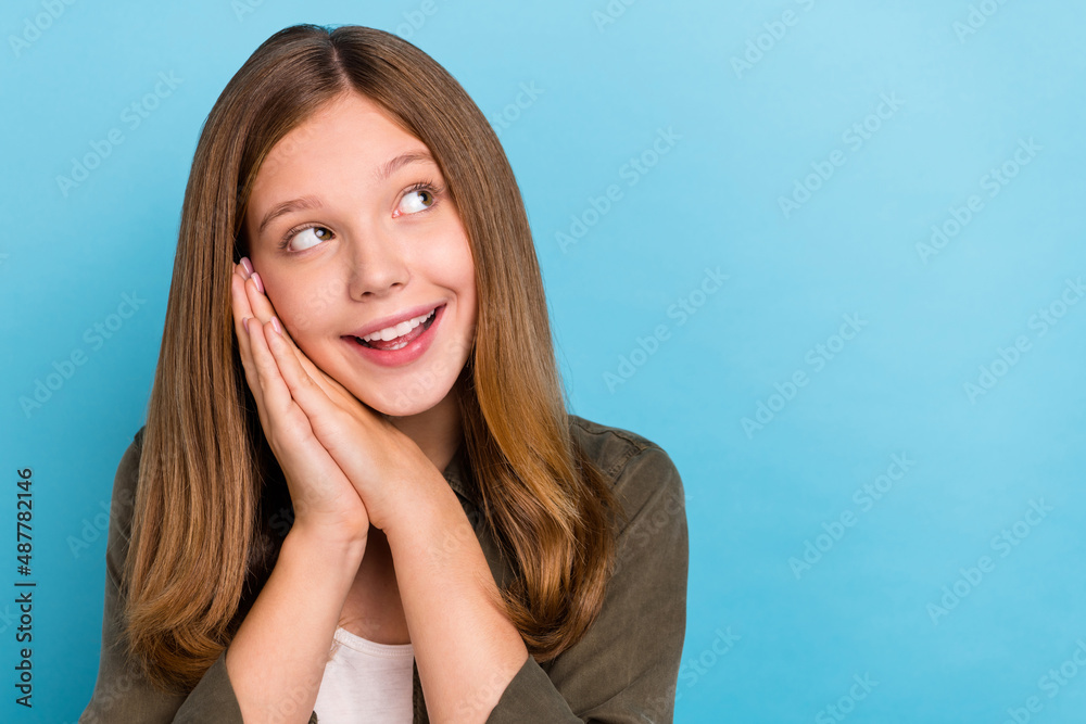 Photo of beautiful good mood teen girl look blank space sleeping hands touch cheek isolated on blue color background Photo of beautiful good mood teen girl look blank space sleeping hands touch cheek isolated on blue color background