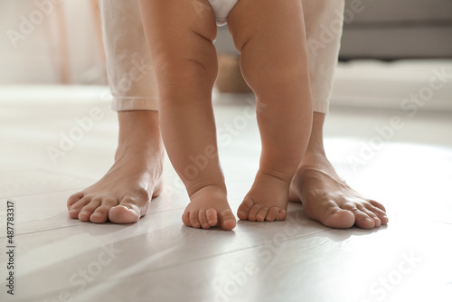 Mother supporting her baby daughter while she learning to walk at home, closeup