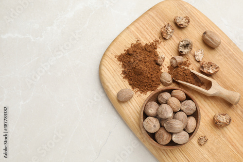 Wooden board with nutmeg powder and seeds on white table, top view. Space for text