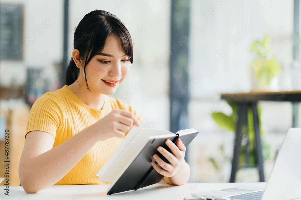 Focused young woman entrepreneur taking notes in notebook while sitting at table with smartphone and cup of drink and working in cafe in daytime Focused young woman entrepreneur taking notes in notebook while sitting at table with smartphone and cup of drink and working in cafe in daytime