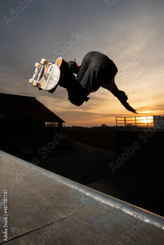 Young skater doing a backside air on a vert ramp at sunset photo