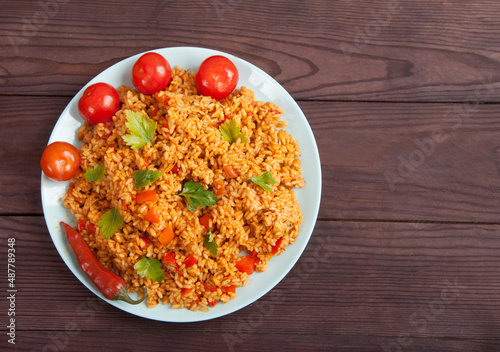 Jollof rice, tomatoes and hot peppers on a blue plate on a wooden background. National cuisine of Africa.