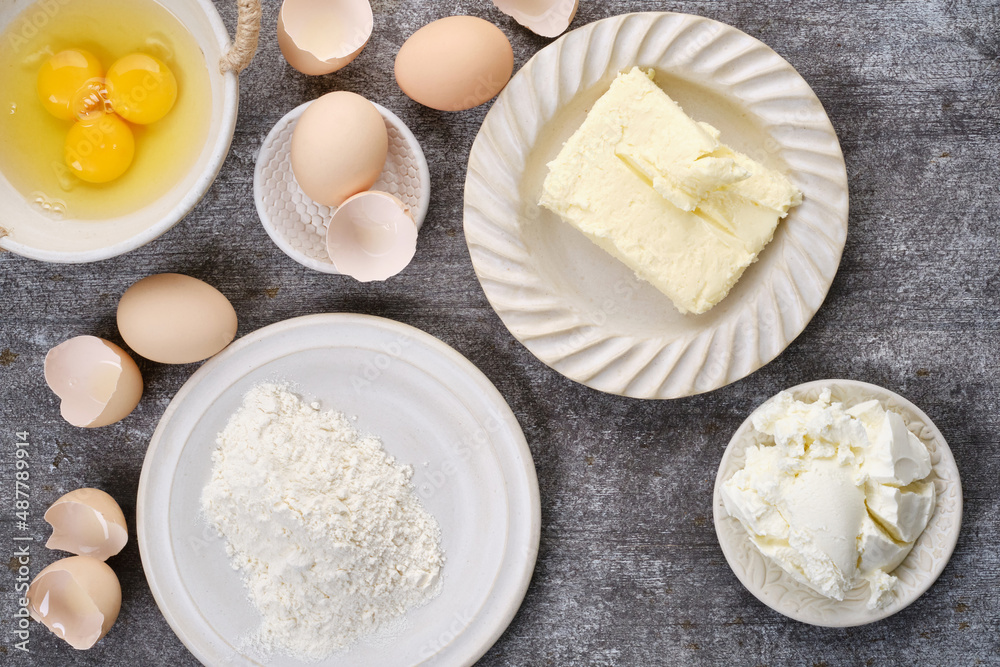 Muffin, baking ingredients: Butter, flour, whole eggs, broken eggs, yolk on a bowl cocoa in plates on the table Muffin, baking ingredients: Butter, flour, whole eggs, broken eggs, yolk on a bowl cocoa in plates on the table